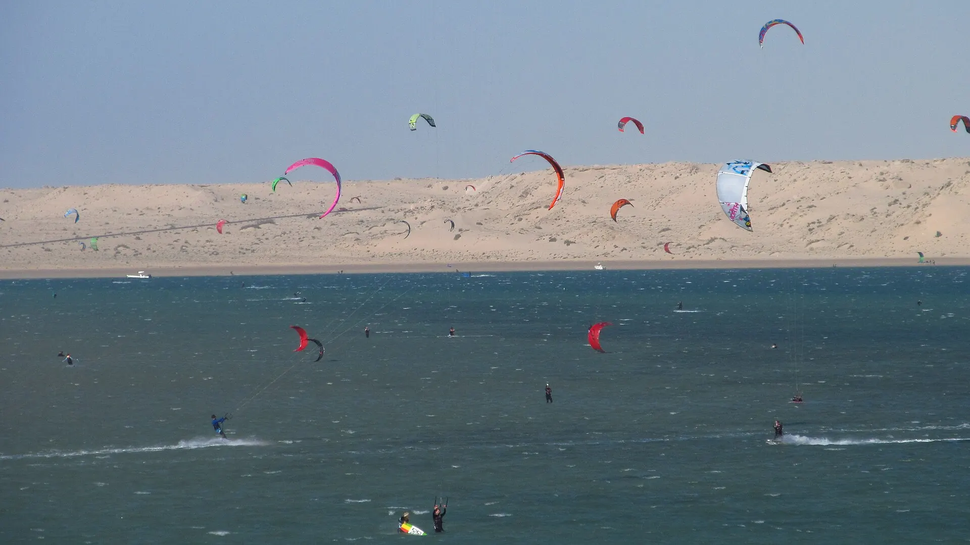 Des dizaines de kitesurfeurs sur la lagune de Dakhla, dunes en arrière-plan